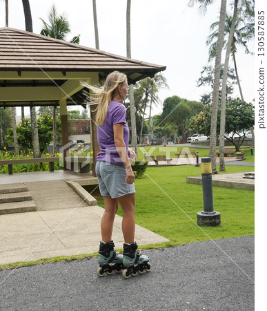 A woman is rollerblading gracefully on a road located in a park A woman is rollerblading gracefully on a road located in a park 130587885