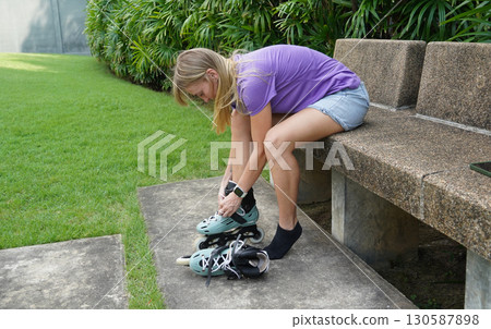 A woman is sitting on a bench and putting on her roller skates 130587898