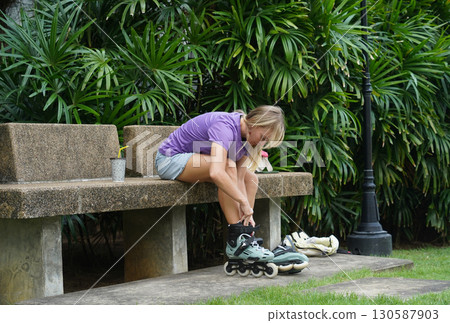 A woman is sitting on a bench and putting on her roller skates A woman is sitting on a bench and putting on her roller skates 130587903