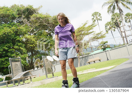 A woman is rollerblading gracefully on a road located in a park 130587904