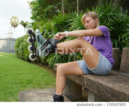 A woman is sitting on a bench and putting on her roller skates 130587905