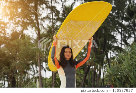 Young woman wearing tight wetsuit is going to surfboard at beautiful beach Young woman wearing tight wetsuit is going to surfboard at beautiful beach 130587937