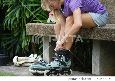 A woman is sitting on a bench and putting on her roller skates 130588030