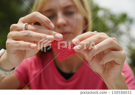 Young woman beading colorful bracelets outdoors in a park 130588031