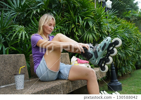 A woman is sitting on a bench and putting on her roller skates 130588042