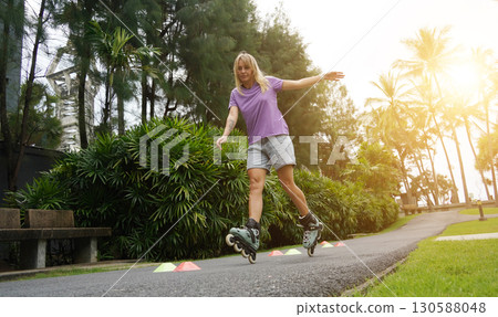 A woman is rollerblading gracefully on a road located in a park 130588048