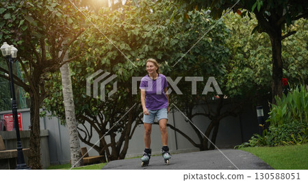 A woman is rollerblading gracefully on a road located in a park 130588051
