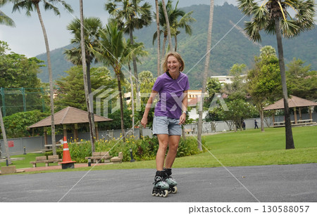 A woman is rollerblading gracefully on a road located in a park 130588057