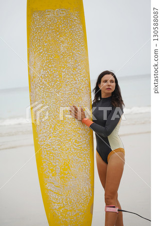 A woman in a stylish wet suit confidently holds a surfboard on the beach A woman in a stylish wet suit confidently holds a surfboard on the beach 130588087