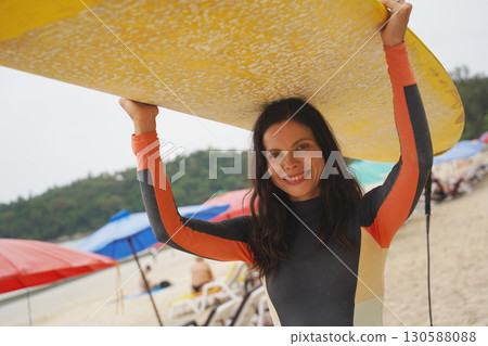 Young woman wearing tight wetsuit is going to surfboard at beautiful beach Young woman wearing tight wetsuit is going to surfboard at beautiful beach 130588088