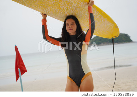 Young woman wearing tight wetsuit is going to surfboard at beautiful beach Young woman wearing tight wetsuit is going to surfboard at beautiful beach 130588089