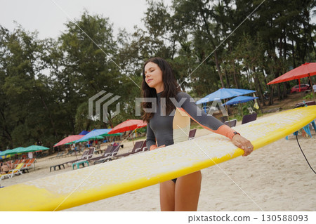 Young woman wearing tight wetsuit is going to surfboard at beautiful beach Young woman wearing tight wetsuit is going to surfboard at beautiful beach 130588093