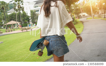 A woman is walking at the city park while carrying a skateboard in her hands 130588099