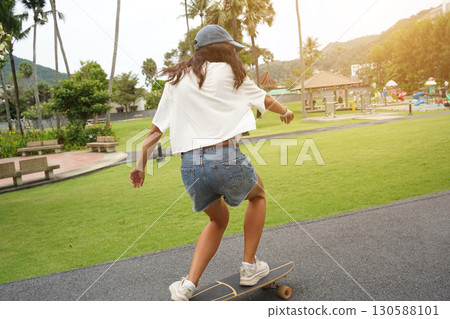 A young woman is skillfully riding a skateboard down a scenic park 130588101