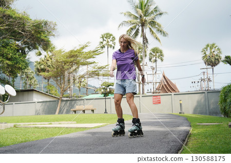 A woman is rollerblading gracefully on a road located in a park 130588175