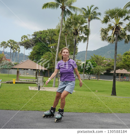 A woman is rollerblading gracefully on a road located in a park 130588184