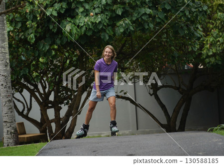 A woman is rollerblading gracefully on a road located in a park A woman is rollerblading gracefully on a road located in a park 130588185