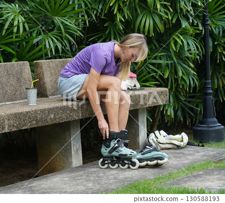 A woman is sitting on a bench and putting on her roller skates A woman is sitting on a bench and putting on her roller skates 130588193