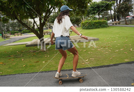 A young woman is skillfully riding a skateboard down a scenic park 130588242