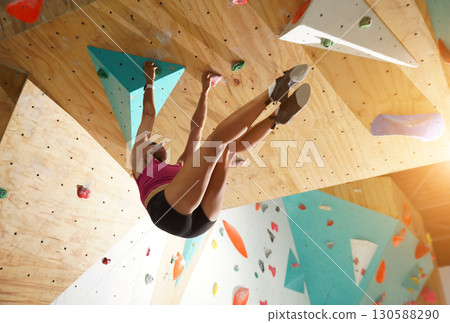 A strong female climber climbs an artificial wall with colorful grips A strong female climber climbs an artificial wall with colorful grips 130588290