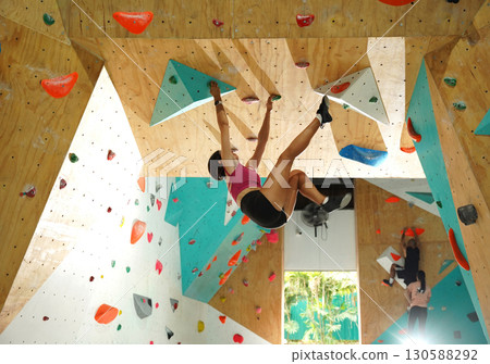 A strong female climber climbs an artificial wall with colorful grips A strong female climber climbs an artificial wall with colorful grips 130588292