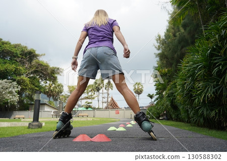 A woman is rollerblading gracefully on a road located in a park A woman is rollerblading gracefully on a road located in a park 130588302