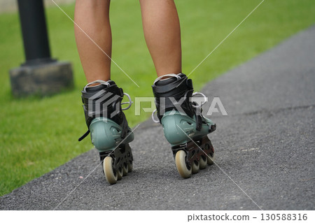 A woman is rollerblading gracefully on a road located in a park 130588316