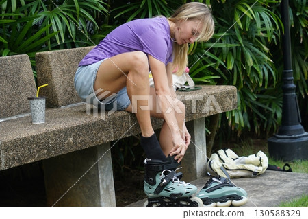 A woman is sitting on a bench and putting on her roller skates A woman is sitting on a bench and putting on her roller skates 130588329