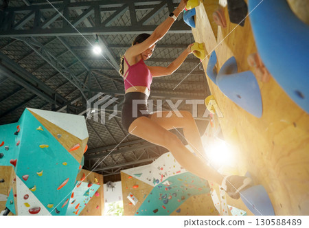 A strong female climber climbs an artificial wall with colorful grips A strong female climber climbs an artificial wall with colorful grips 130588489