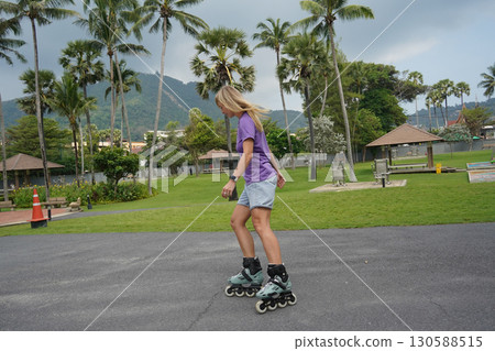 A woman is rollerblading gracefully on a road located in a park 130588515