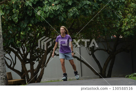 A woman is rollerblading gracefully on a road located in a park A woman is rollerblading gracefully on a road located in a park 130588516