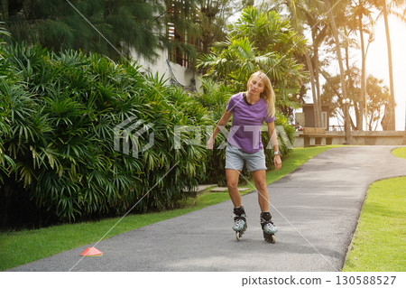 A woman is rollerblading gracefully on a road located in a park 130588527