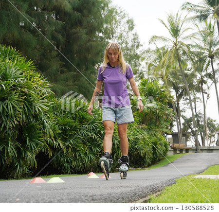 A woman is rollerblading gracefully on a road located in a park 130588528