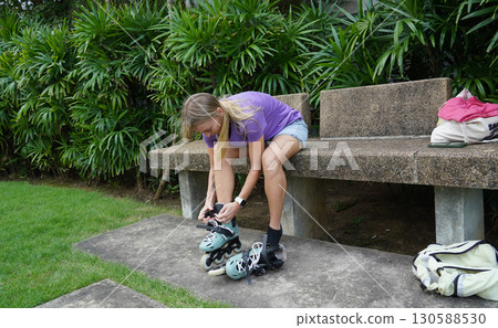 A woman is sitting on a bench and putting on her roller skates 130588530