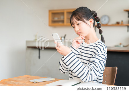 Elementary and junior high school girls using smartphones in the living room and dining room at home 130588539