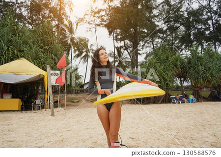 Young woman wearing tight wetsuit is going to surfboard at beautiful beach 130588576