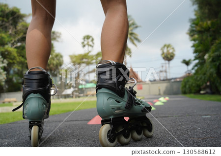 A woman is rollerblading gracefully on a road located in a park 130588612