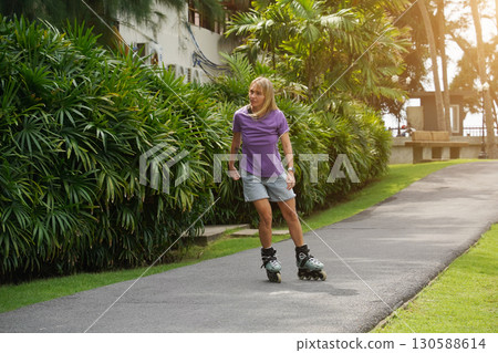 A woman is rollerblading gracefully on a road located in a park A woman is rollerblading gracefully on a road located in a park 130588614