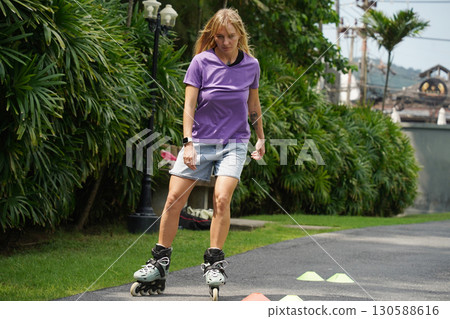 A woman is rollerblading gracefully on a road located in a park A woman is rollerblading gracefully on a road located in a park 130588616