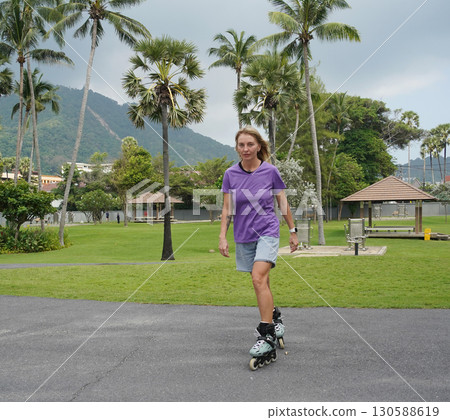 A woman is rollerblading gracefully on a road located in a park 130588619