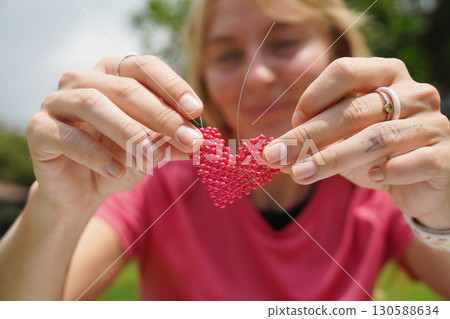 Young woman beading colorful bracelets outdoors in a park 130588634