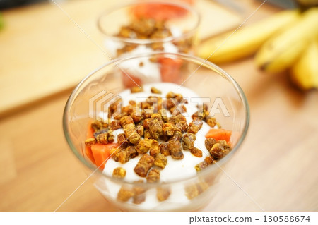 Two glasses of vegetarian yogurt dessert with papaya and granola on a wooden table Two glasses of vegetarian yogurt dessert with papaya and granola on a wooden table 130588674