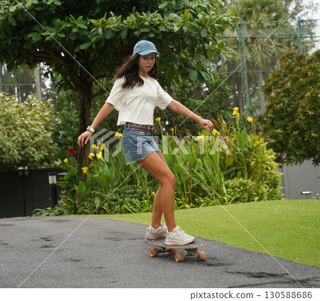 A young woman is skillfully riding a skateboard down a scenic park 130588686