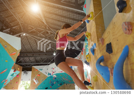 A strong female climber climbs an artificial wall with colorful grips 130588698