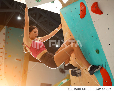 A strong female climber climbs an artificial wall with colorful grips A strong female climber climbs an artificial wall with colorful grips 130588706