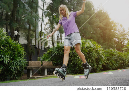A woman is rollerblading gracefully on a road located in a park 130588728