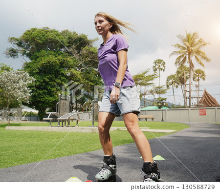 A woman is rollerblading gracefully on a road located in a park 130588729