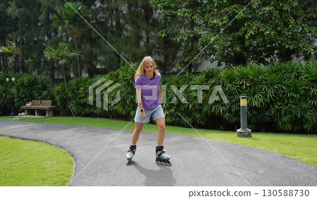 A woman is rollerblading gracefully on a road located in a park 130588730