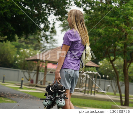 A woman is rollerblading gracefully on a road located in a park A woman is rollerblading gracefully on a road located in a park 130588736