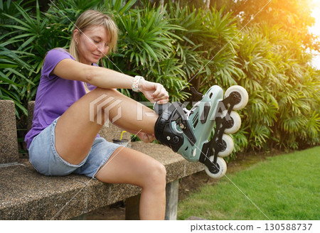 A woman is sitting on a bench and putting on her roller skates 130588737